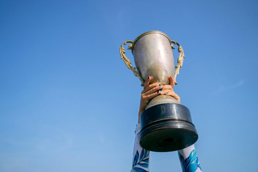 Hands holding a trophy high against a clear blue sky, symbolizing victory and success.